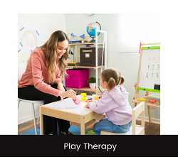 A woman smiles while giving a toy to a child. Learn how a therapist in Fair Oaks, CA can support your child with therapy for children in Roseville, CA today. They can harness the healing power of play therapy and more!