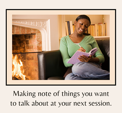 A black woman smiles while writing in a journal in front of a fireplace. The text below says making note of things you want to talk about at your next session. Learn how a therapist in Fair Oaks, CA can offer support via counseling in Roseville, CA.