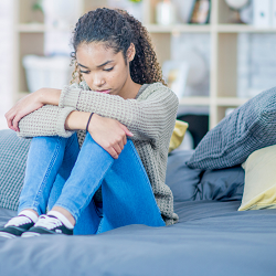 Teen girl sits on the floor hugging knees looking upset representing how teen therapy in Fair Oaks,. CA and teen therapy in Roseville, CA at the Relationship Therapy Center can help.