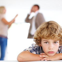 young boy in the foreground looks upset as parents argue in the background representing the stress kids can feel is exes cant work together and parent. Get co-parenting counseling in Fair Oaks, CA and co-parenting counseling in Roseville, CA