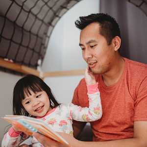 father reads a book with his young child before bed. He works on coparenting skills in coparenting counseling in Fair Oaks, CA and coparenting counseling in Roseville, CA with an online therapist in California at the Relationship Therapy Center