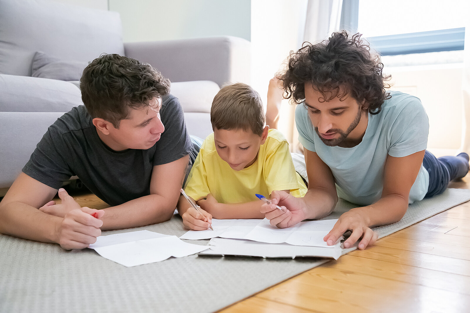 gay couple sits with their son doing homework on the floor representing the benefits of getting family therapy in Fair Oaks, CA or family therapy in Roseville, CA with a family therapist at the Relationship Therapy Center