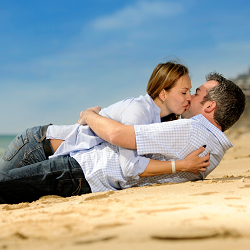 A couple laying in the sand kissing representing how a couples retreat in California can help couples reconnect.