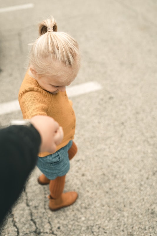 Blond toddler holding her parent’s hand