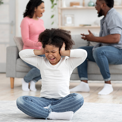 A child covers her ears while their parents argue behind her. Trauma therapy in Roseville, CA can offer support for past trauma. Learn more about overcoming PTSD in Roseville, CA by contacting a therapist for teens in Roseville, CA.