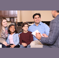 A family smiles as they listen to a person with a clipboard. Learn more about the support family therapy in Sacramento, CA can offer. Search family counseling Fair Oaks, CA today or search counseling near me to learn more.