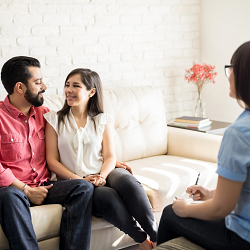 A couple smile with one another as a therapist listens with a notepad. A marriage counselor in California can offer support with online marriage counseling in California and other services. 95678