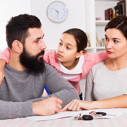 young girl embraces both of her parents who look upset while signing papers representing the hardships that come from coparenting. Learn how to parent together in co-parenting counseling in Fair Oaks, CA and co-parenting counseling in Roseville, CA