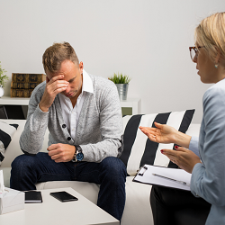 A man holds touches their forehead while a woman talks to them. This could represent counseling in Roseville, CA and the support an anxiety therapist in Fair Oaks, CA can offer. Search “counseling near me” to learn more today.