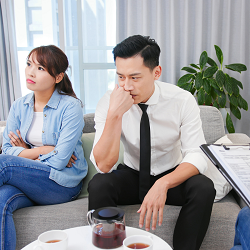 A couple avoid eye contact as they sit across from someone holding a clipboard. This could represent meeting with a therapist in Fair Oaks, CA. Learn more about online marriage counseling in California, couples therapy retreats in California, & more.