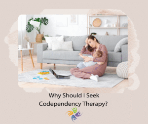 Why Should I Seek Codependency Therapy?  Image of an exhausted woman sitting on the floor, holding a toddler, with a laptop and notebook sitting on the floor. For codependency therapy, both in-person and online, contact The Relationship Therapy Center in Sacramento, Roseville and Fair Oaks California.